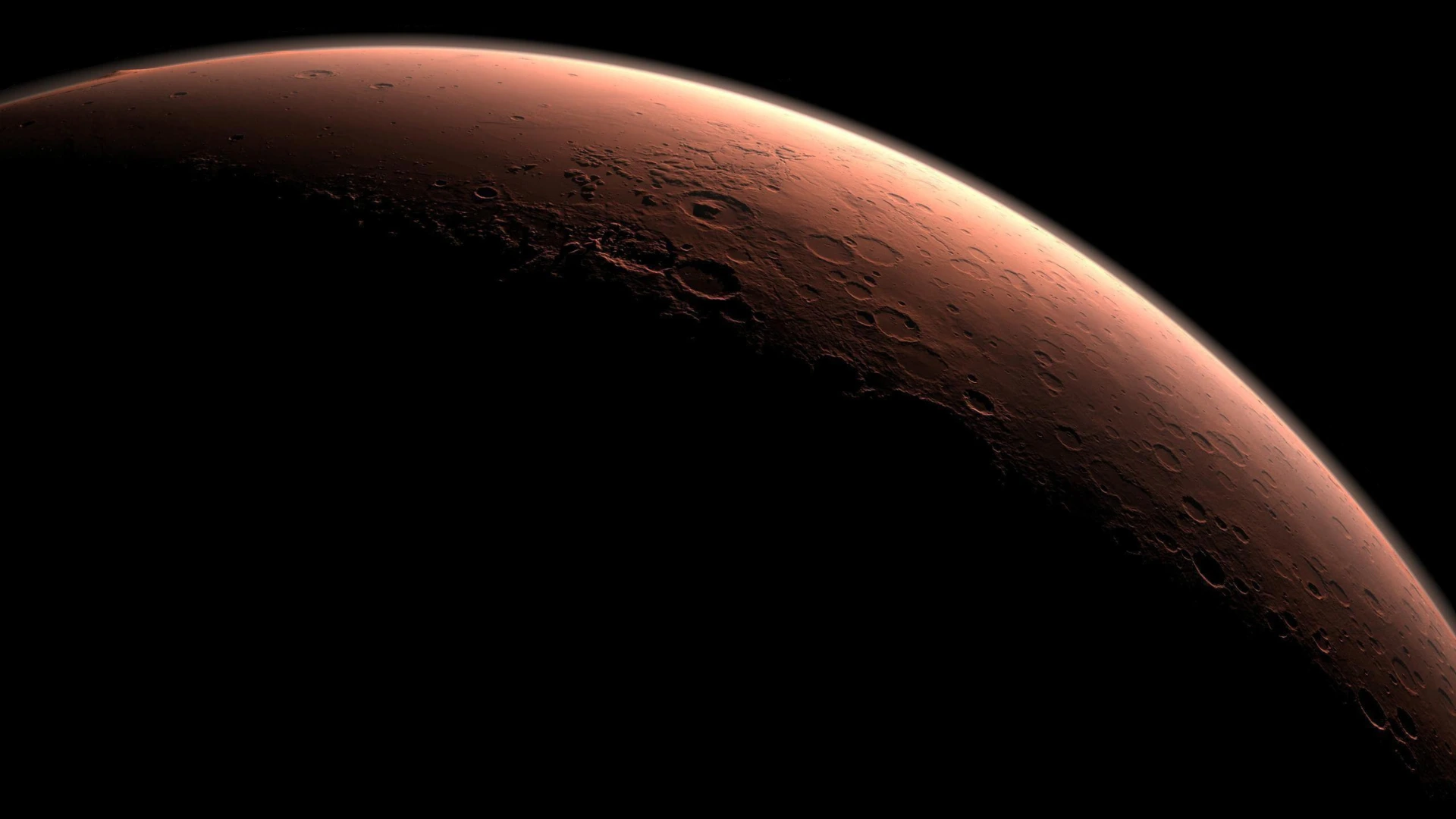 Fotografia em close-up da curvatura do planeta Marte, mostrando sua superfície vermelha e repleta de crateras, iluminada por uma luz lateral dramática contra o vazio negro do espaço.